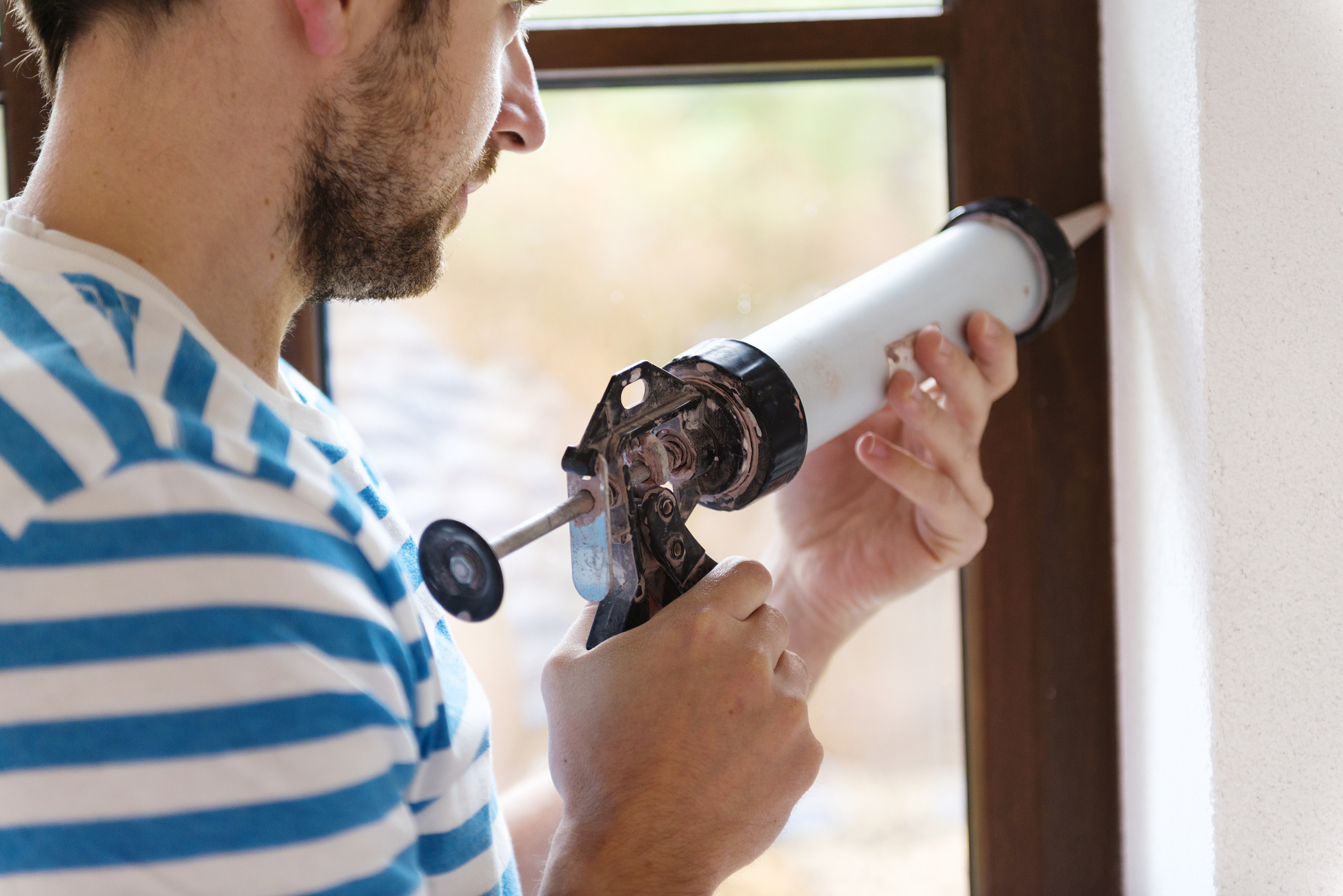 Man uses silicone to caulk window. 